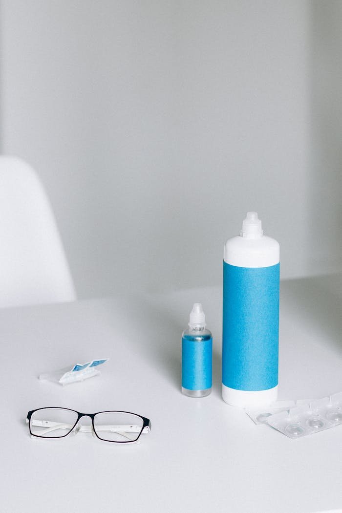 Eyeglasses and contact lens solution bottles on a white table.